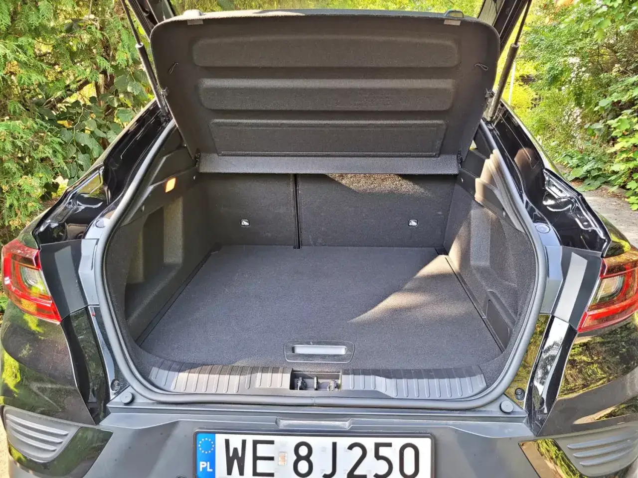 Otwarty bagażnik czarnego Renault Arkana. Wnętrze jest puste i czyste, gotowe na podróż. Wiele osób chwali to auto w swoich renault arkana opinie.