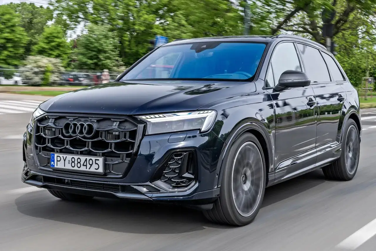 Ciemny Audi Q7 w ruchu ulicznym, z widocznym grillem i reflektorami. Jego imponujące audi q7 wymiary sugerują przestronne wnętrze i stabilność na drodze.