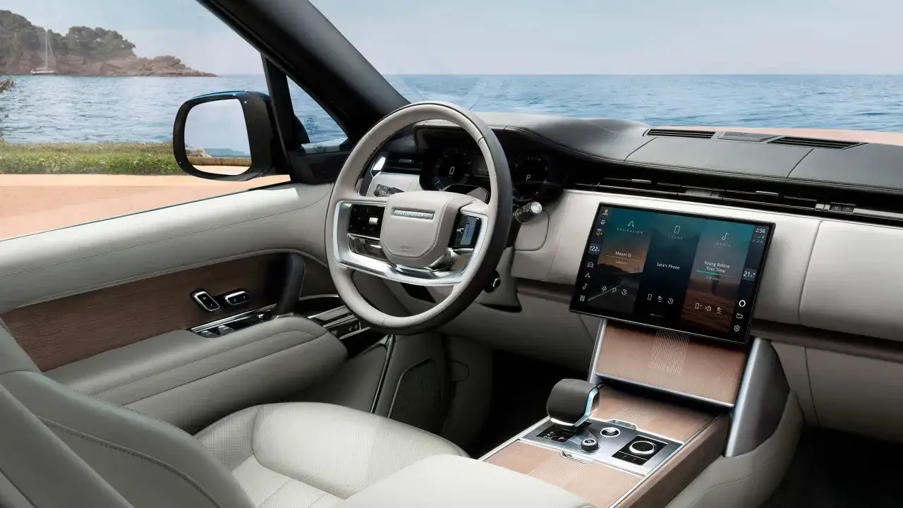 Wnętrze Range Rover Autobiography z widokiem na morze. Jasna skóra, drewniane akcenty i nowoczesny ekran.
