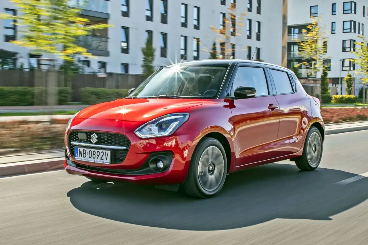 Czerwony Suzuki Swift z czarnym dachem pędzi ulicą. Wiele osób chwali jego zwinność, co potwierdzają liczne suzuki swift opinie.