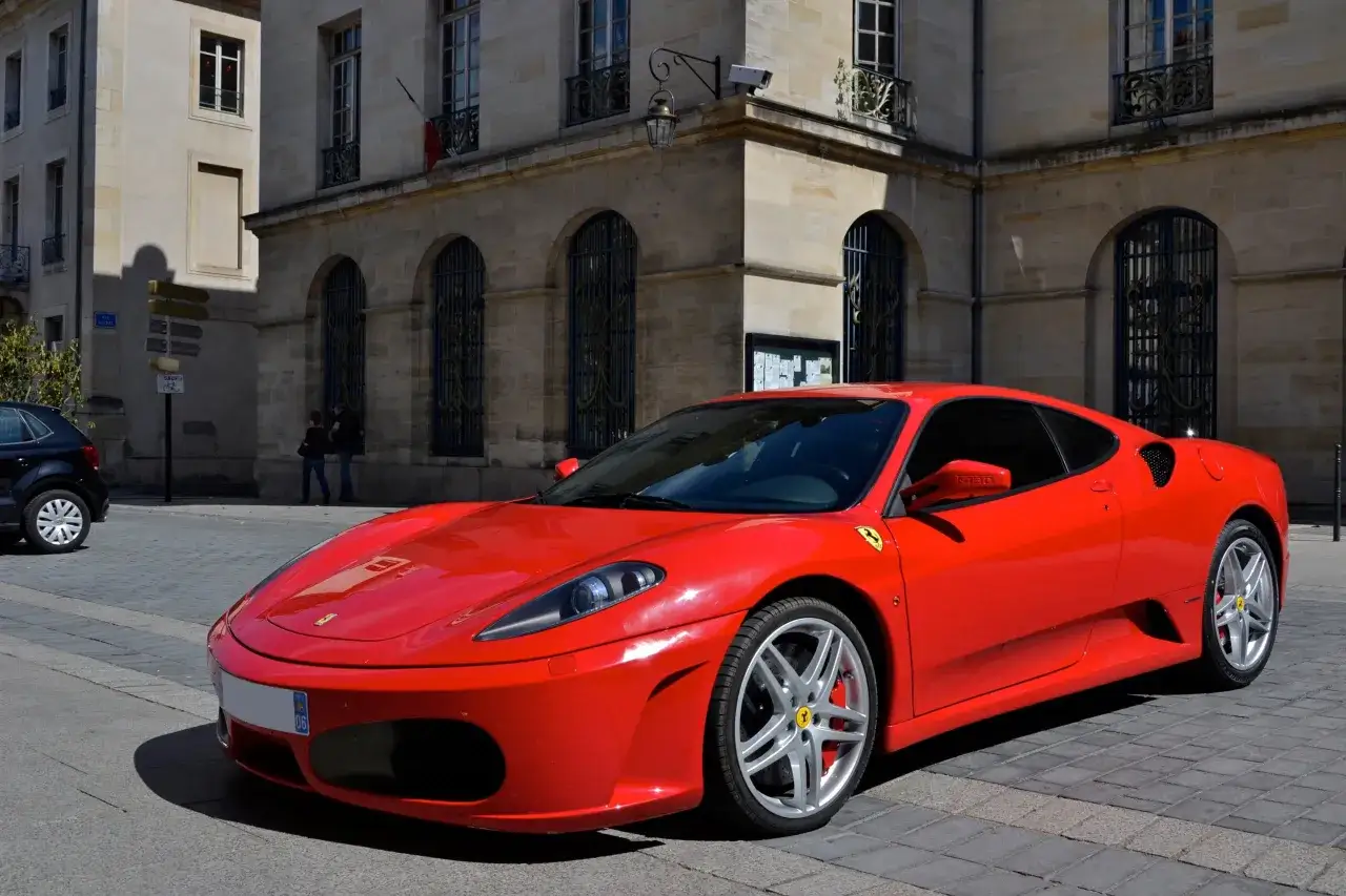 Czerwone Ferrari F430 na bruku przed kamienicą. Zastanawiasz się, ile kosztuje Ferrari? To marzenie wielu kierowców.