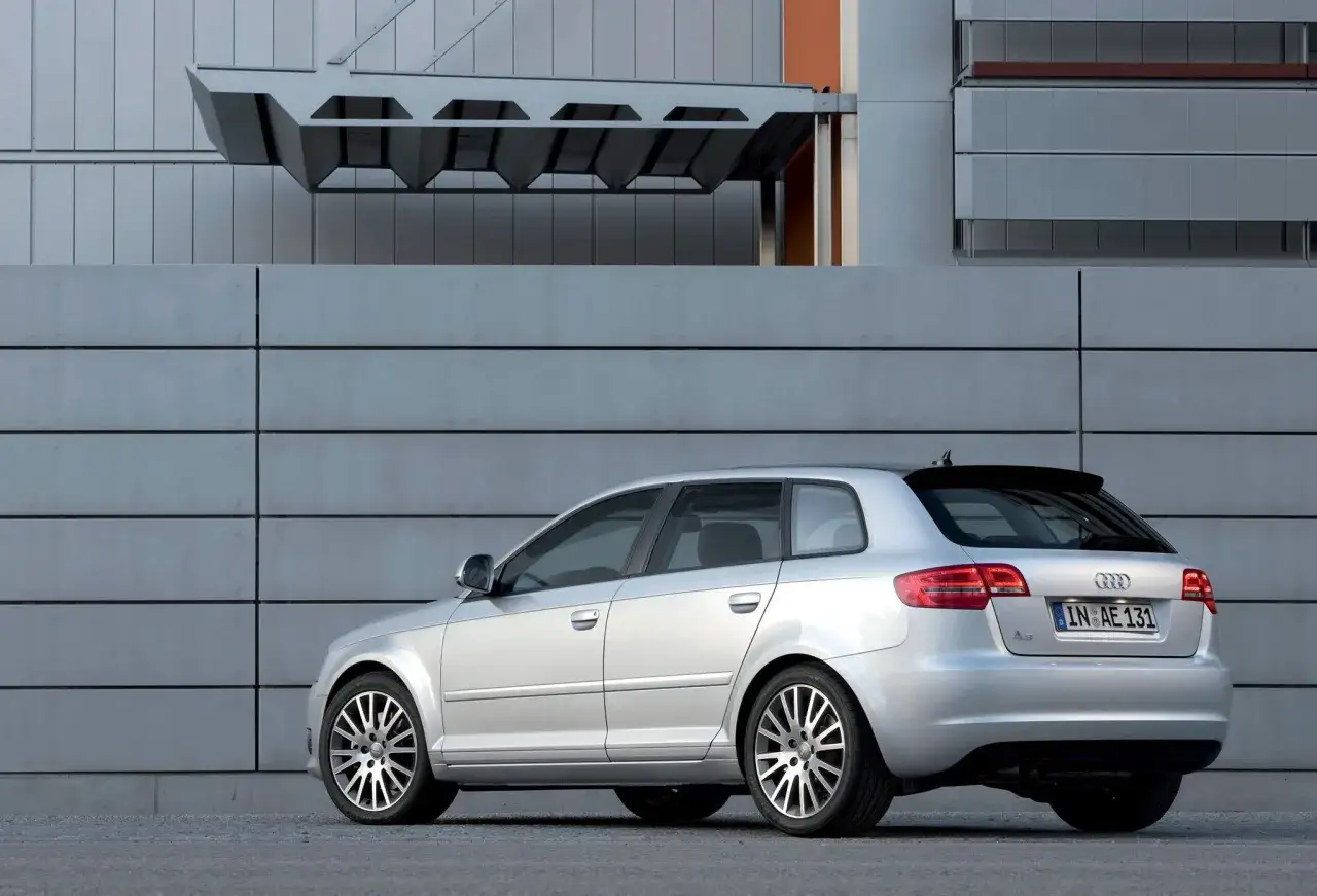 Srebrne Audi A3 8P Sportback zaparkowane przy nowoczesnym budynku z metalową fasadą.