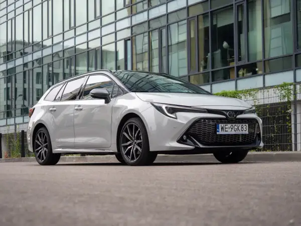 Biała Toyota Corolla 2.0 Hybrid na tle nowoczesnego budynku.