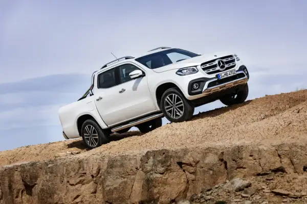 Biały mercedes pickup zjeżdża po piaszczystym zboczu, demonstrując swoje możliwości terenowe.