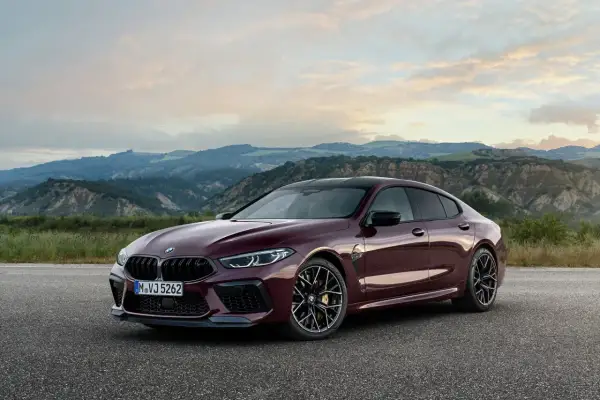 Eleganckie BMW M8 w kolorze głębokiej wiśni, zaparkowane na tle malowniczych, pofałdowanych wzgórz o zachodzie słońca.