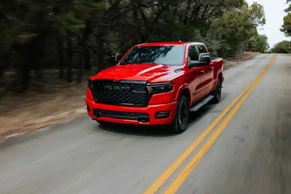 Czerwony Dodge Ram 1500 pędzi po krętej drodze wśród drzew.