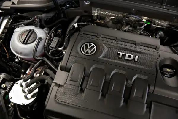 Silnik 2.0 TDI 140KM Volkswagena. Widoczny zbiornik płynu chłodniczego i osłona silnika z logo TDI.