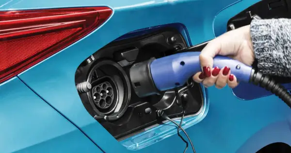 Dłoń z czerwonym lakierem na paznokciach podłącza ładowarkę do niebieskiej hybrydy plug-in.