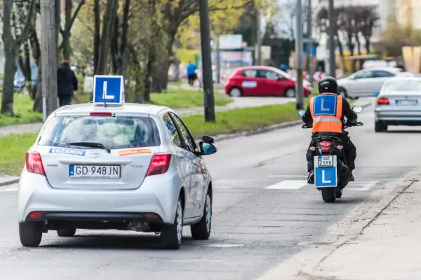 Nauka jazdy na motorowerze, czyli ile kosztuje prawo jazdy AM. Na drodze auto z literą "L" i motocyklista z kamizelką odblaskową.