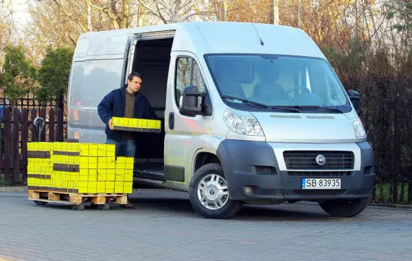 Mężczyzna rozładowuje żółte paczki z furgonetki Fiat Ducato 2.3.