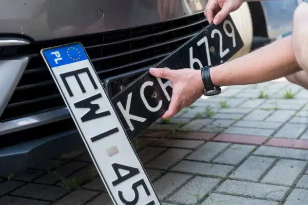 Ręce montują tablicę rejestracyjną do samochodu. Nowa elc rejestracja czeka na zamontowanie.