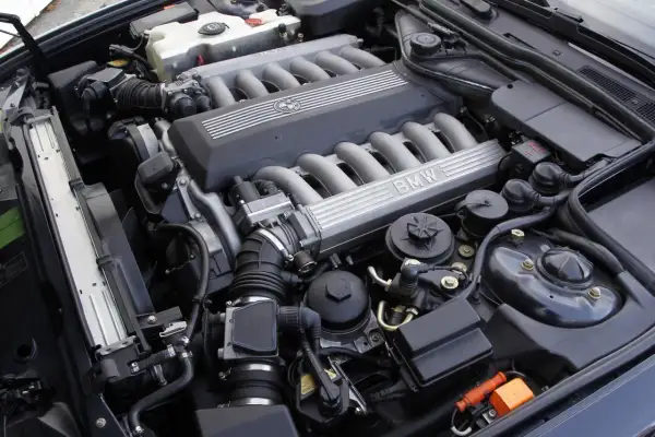 Silnik V12 BMW z widocznymi kolektorami dolotowymi i pokrywą z logo marki.