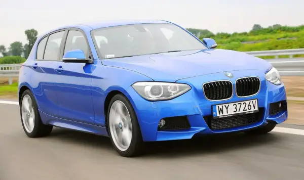 Niebieskie BMW 118d pędzi po drodze, ukazując dynamiczny design i sportowy charakter.