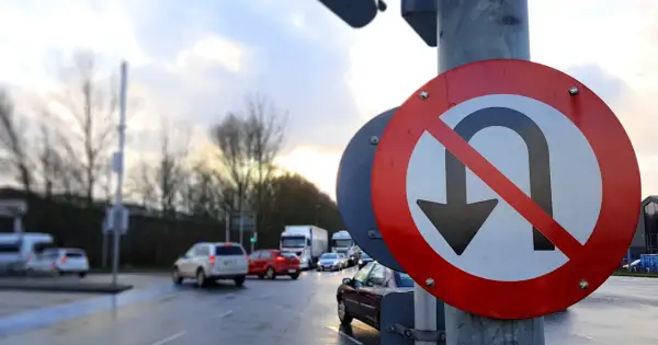 Znak zakazu zawracania na skrzyżowaniu. Samochody stoją w deszczu, czekając na zielone światło.
