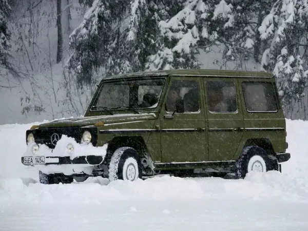 Zielony Mercedes G-klasa z napędem **awd** przebija się przez zaspy w zaśnieżonym lesie.