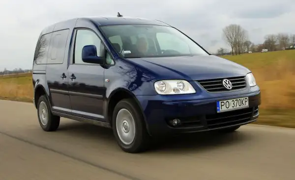 Ciemnoniebieski Volkswagen Caddy 3 w ruchu drogowym, z widocznym kierowcą.