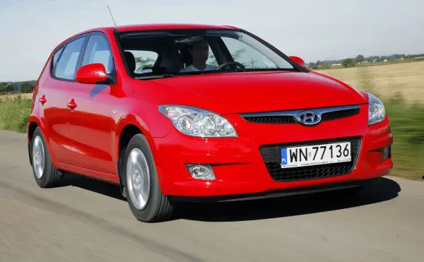 Czerwony Hyundai i30 1.6 CRDi jedzie po drodze wśród pól.