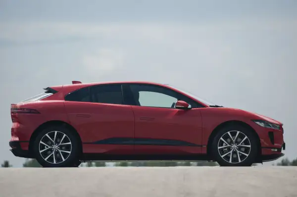 Czerwony jaguar elektryczny w profilu, z widokiem na jego aerodynamiczną sylwetkę i felgi.