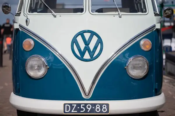 Przód klasycznego VW T2 w kolorze białym i niebieskim. Charakterystyczne okrągłe logo VW i okrągłe reflektory.