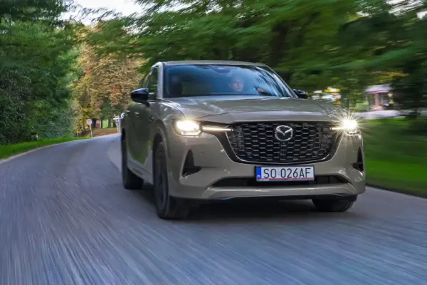Nowa Mazda CX-60 3.3 diesel sunie po krętej drodze wśród zieleni.